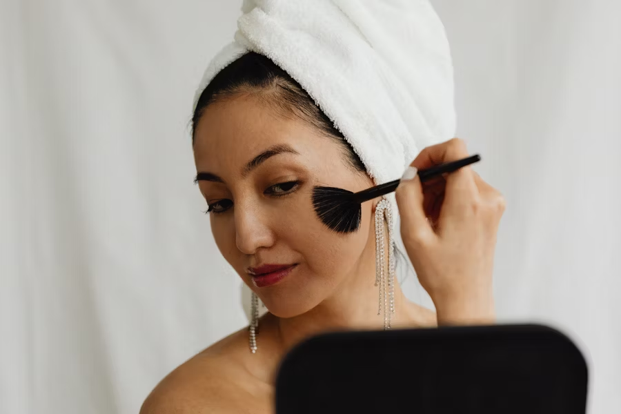 a-woman-with-a-towel-on-her-head-brushes-her-face-with-a-brush