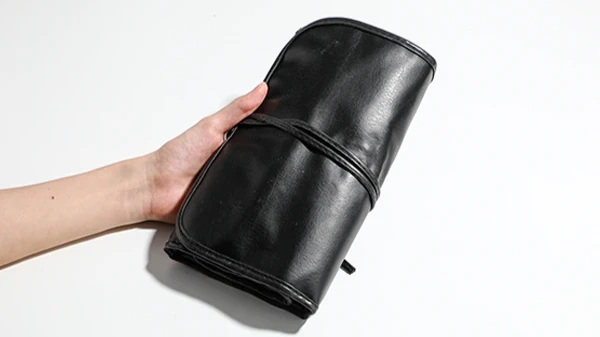 Black leather roll-up makeup brush packaging holder held by a hand.