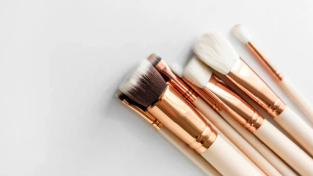 Close-up view of makeup brushes with rose gold ferrules and soft bristles arranged diagonally on a bright surface.